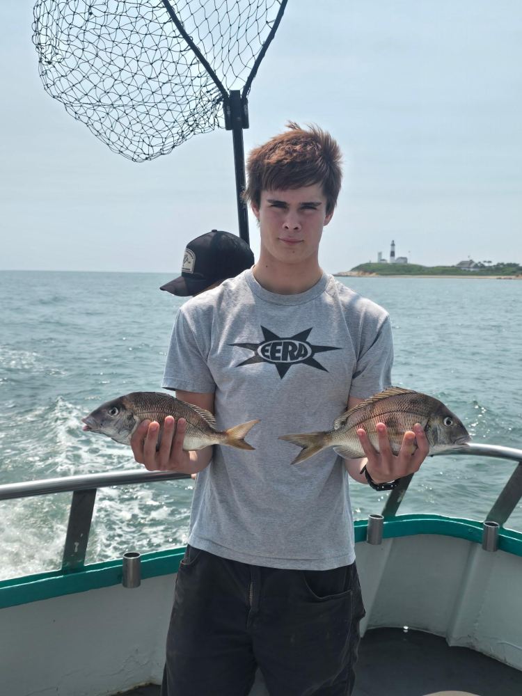 Person on a boat holding two fish with a net and ocean in the background.