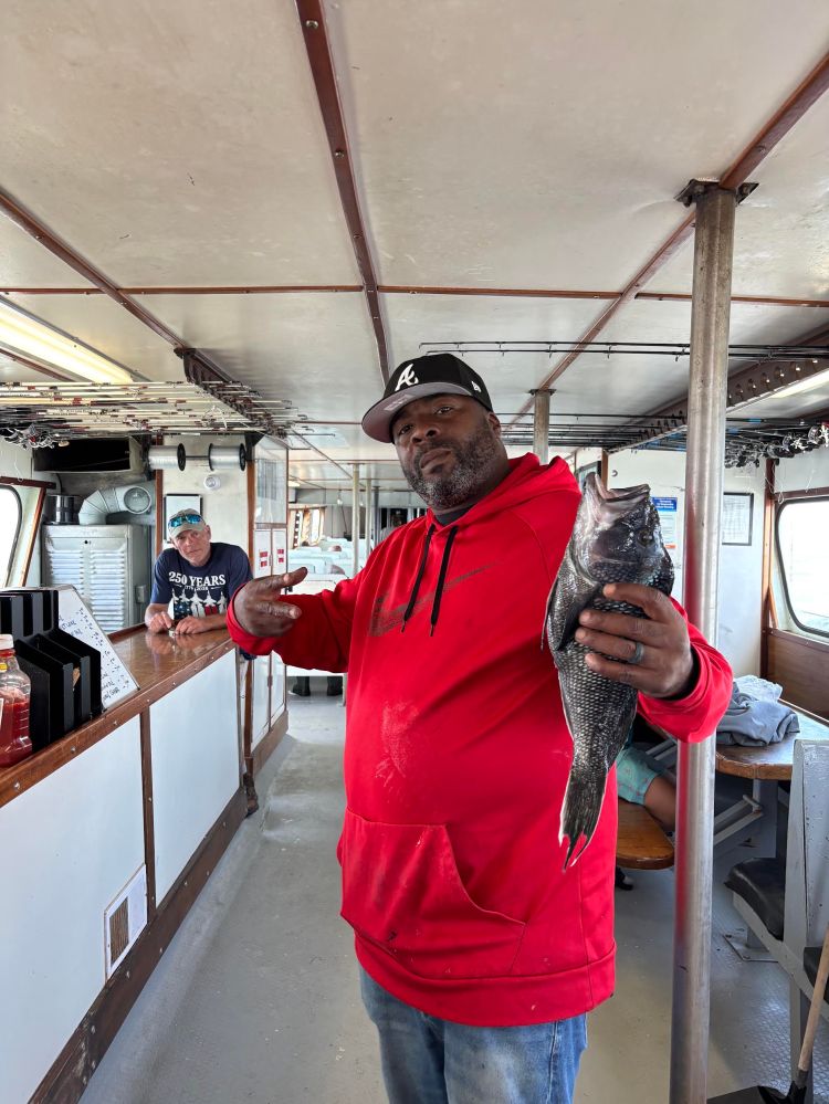 Man in red hoodie holding a fish inside a boat cabin.