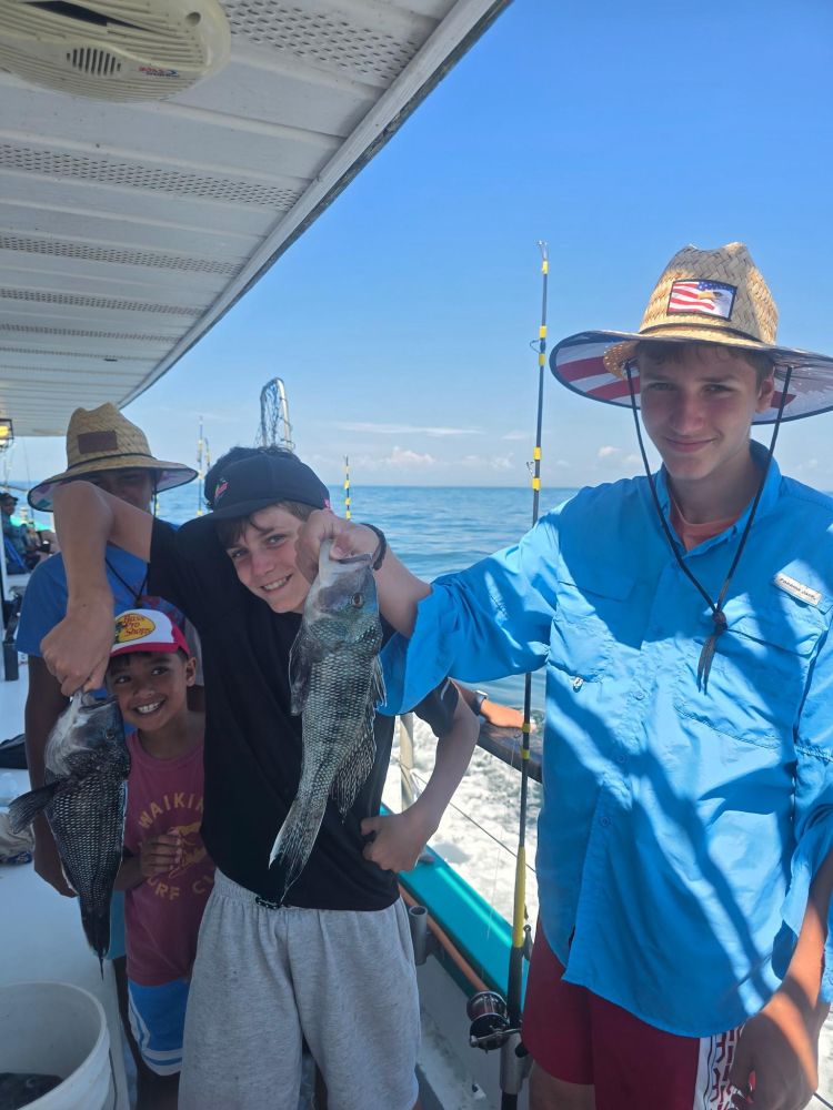 Three boys on a boat holding fish, smiling under a clear blue sky.
