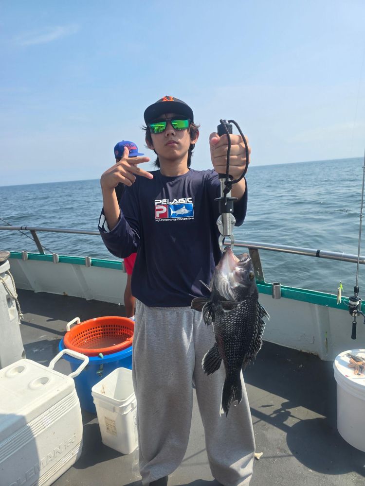 Person on a boat holding a large fish, wearing sunglasses and a cap.