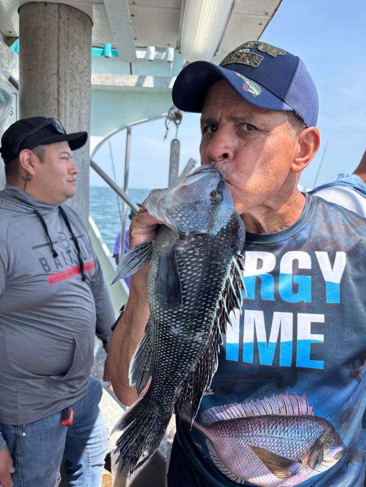 Man kissing a fish on a boat, wearing a cap and graphic t-shirt.