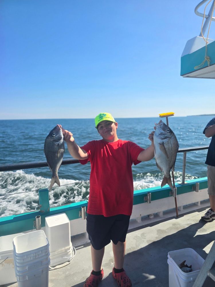 Child on boat holding two fish, wearing a bright cap and red shirt.