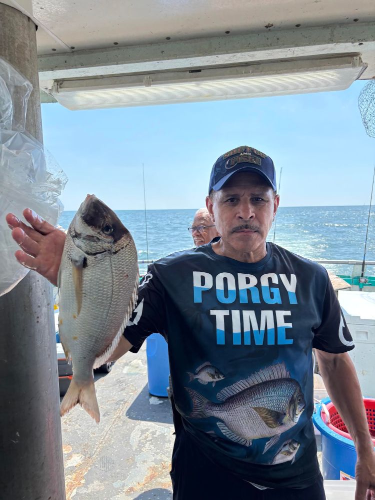 Man holding a fish on a boat, wearing a shirt with 'PORGY TIME' text.