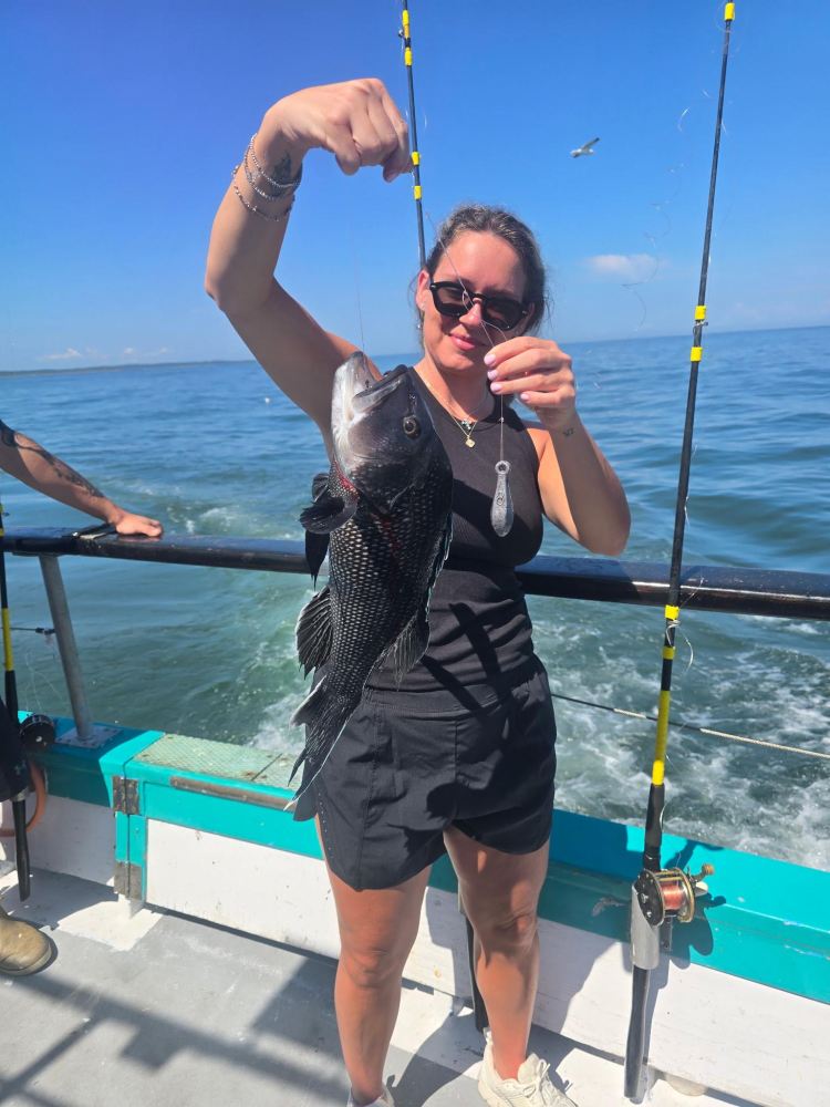 Woman on boat holding a large fish, with fishing rods and ocean in background.