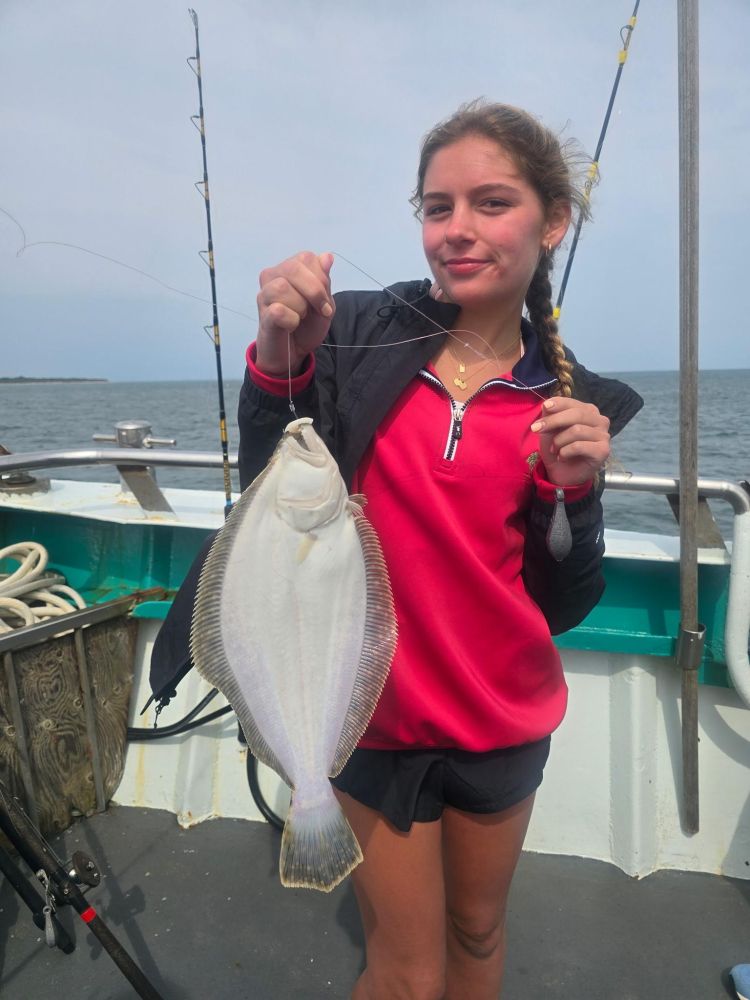 Person on a boat holding a large fish, with fishing rods in the background.