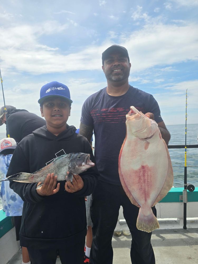 Man and boy on boat holding large fish with rods in background.