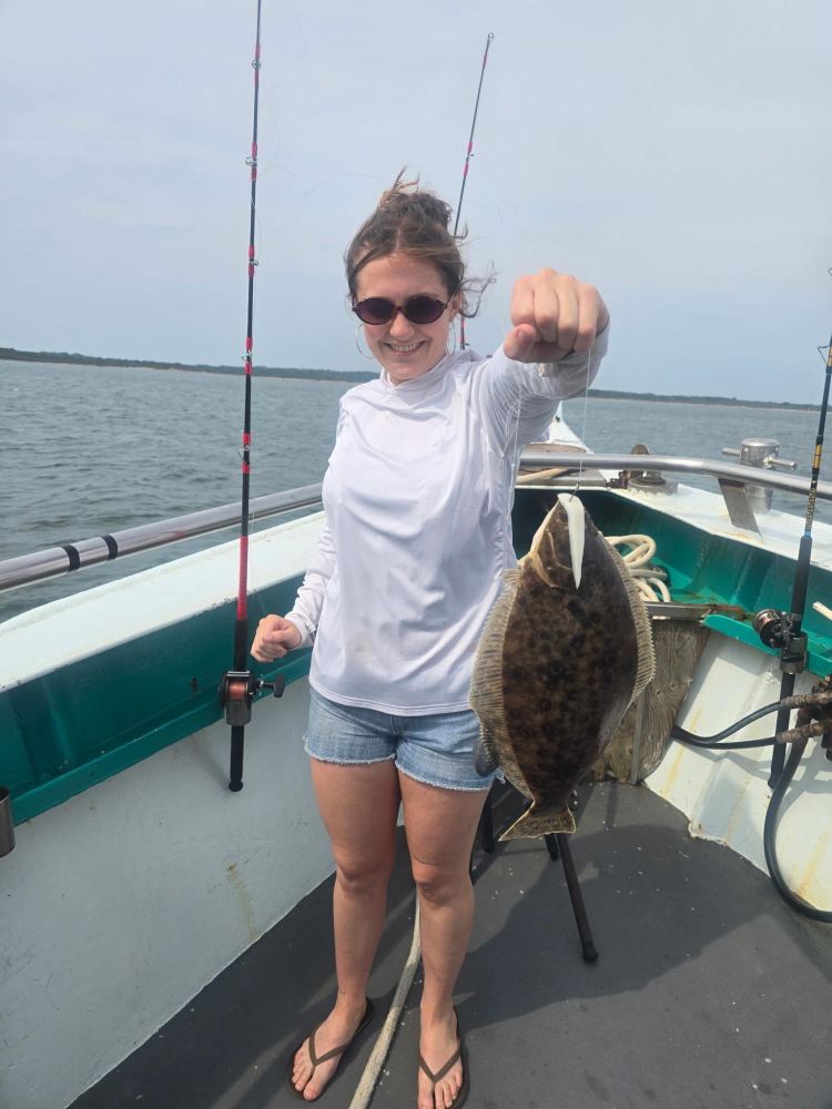 Person on a boat holding a flat fish, wearing sunglasses and a white shirt.