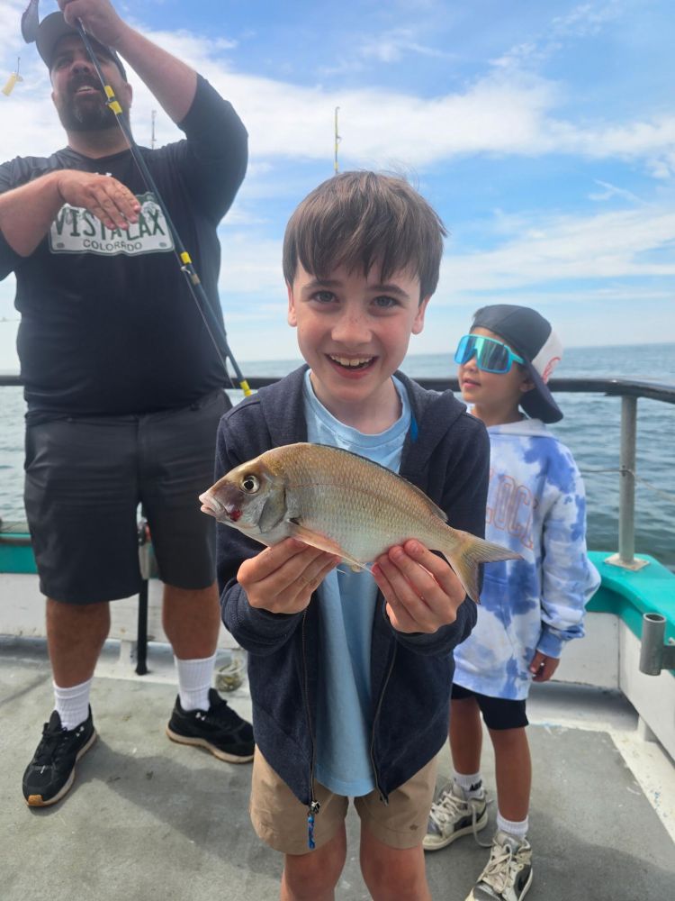Boy holding a fish on a boat with two people in the background.