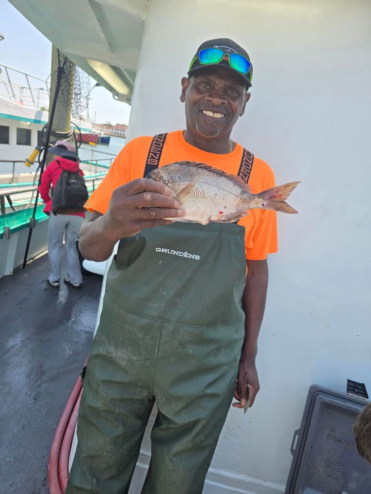 Person in fishing gear holding a fish on a boat deck.