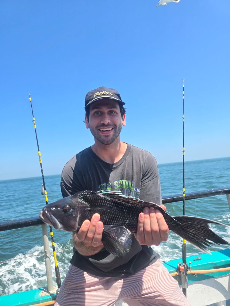 Man holding a black fish on a boat with fishing rods, ocean in background.