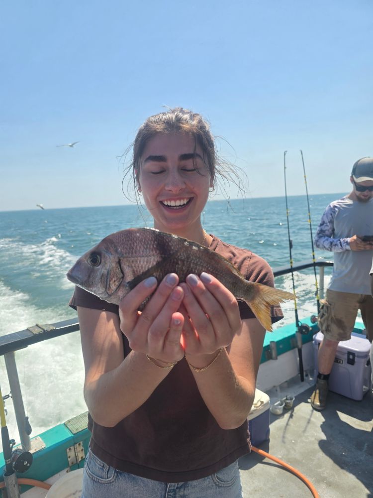 Person smiling and holding a fish on a boat with ocean in the background.