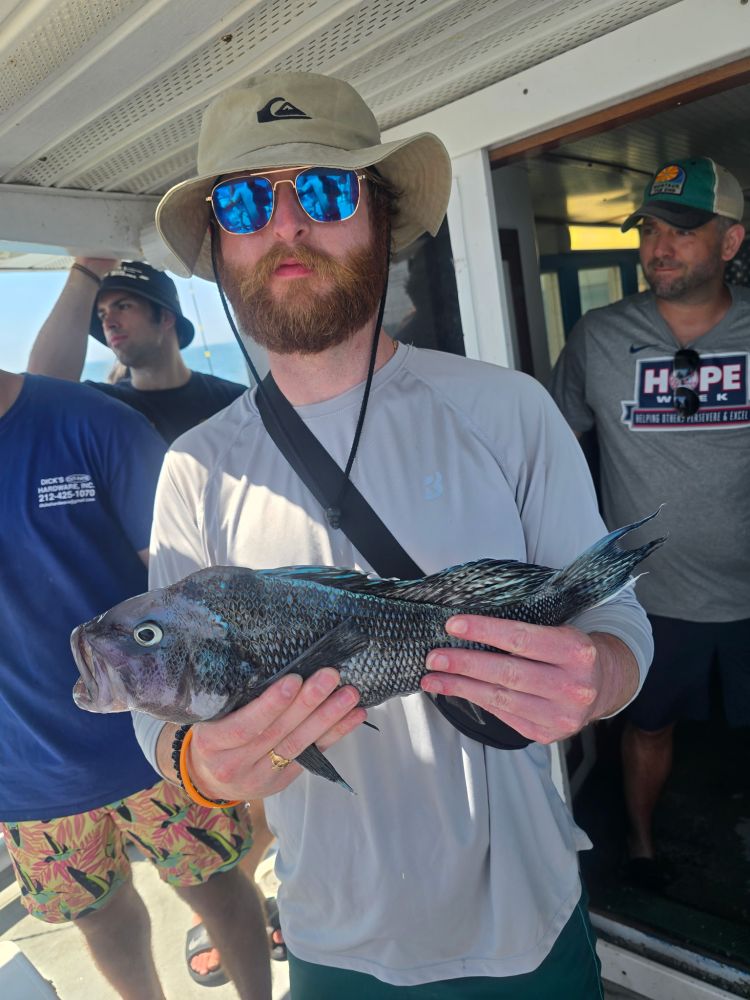 Man holding a large fish on a boat, wearing sunglasses and a bucket hat.