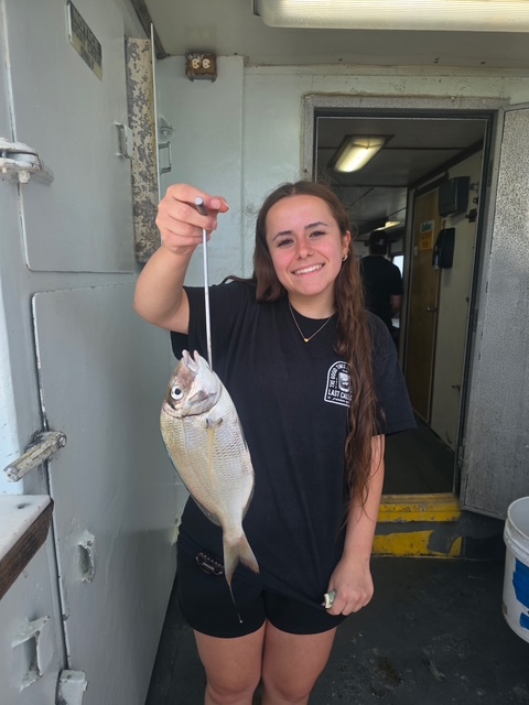 Person smiling, holding a fish on a boat next to a door.