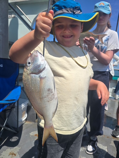 Child smiling, holding a fish on a boat with others nearby.