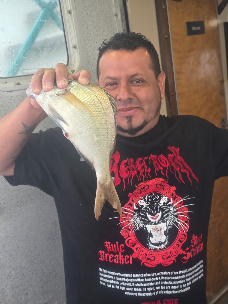 Man holding a fish up to his face, smiling, wearing a black shirt with red text.