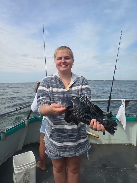 Person holding a fish on a boat with fishing rods in the background.