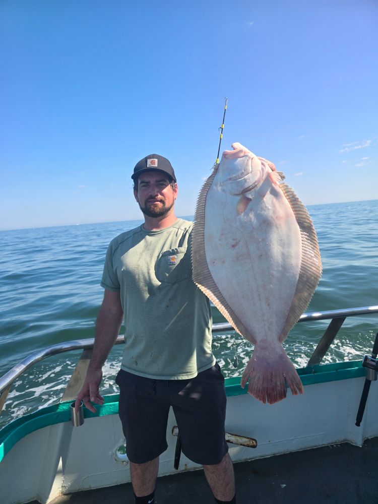 Man on boat holding large fish with ocean backdrop.