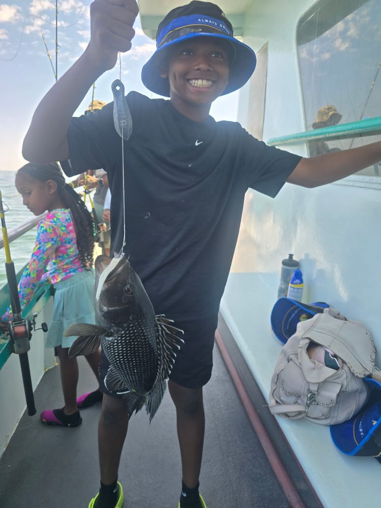 Smiling boy in a hat holding a fish on a boat, with a girl in the background.