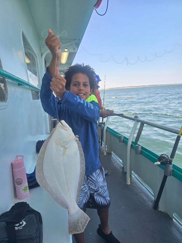 Child holding a large fish on a boat with a calm sea in the background.