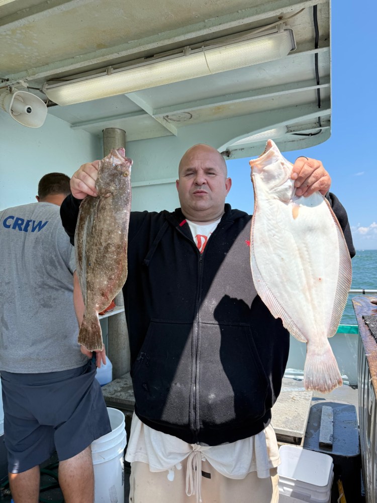 Man holding two fish on a boat deck, blue sky in background.