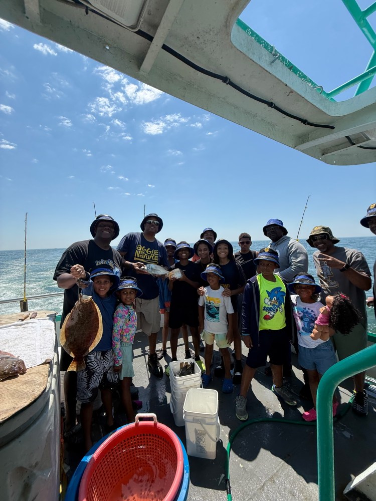 Group of people fishing on a boat, holding a fish, under a clear sky.