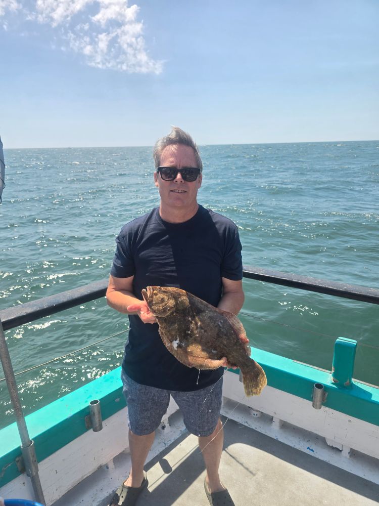 Person holding a fish on a boat with ocean in the background.