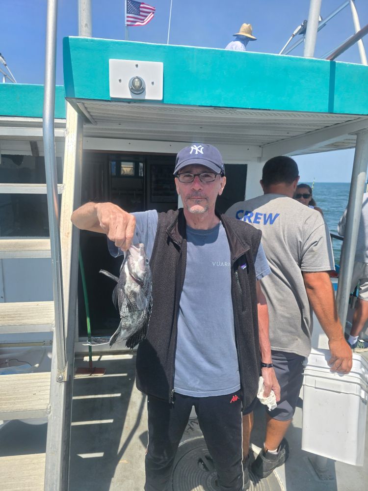 Man holding a fish on a boat with crew member nearby.