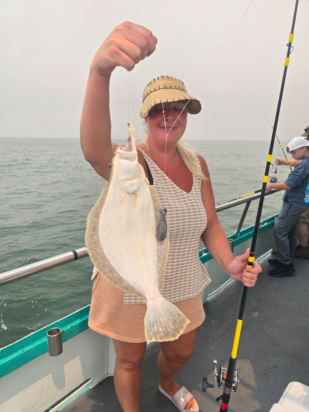 Person on a boat holding a caught fish with a fishing rod.