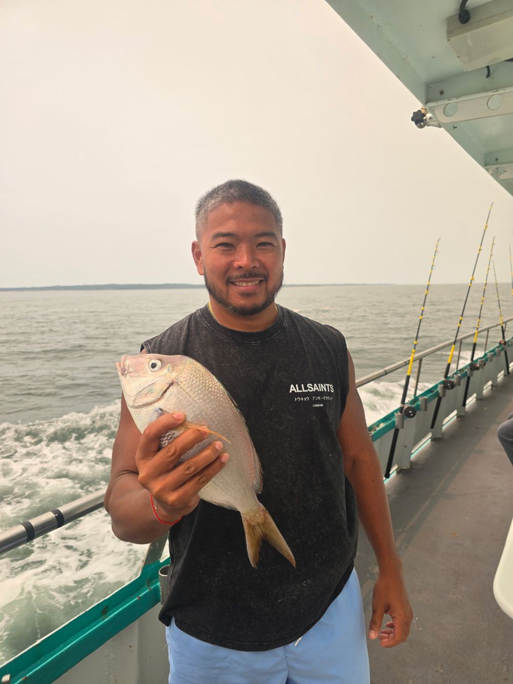 Man holding fish on boat with ocean backdrop.