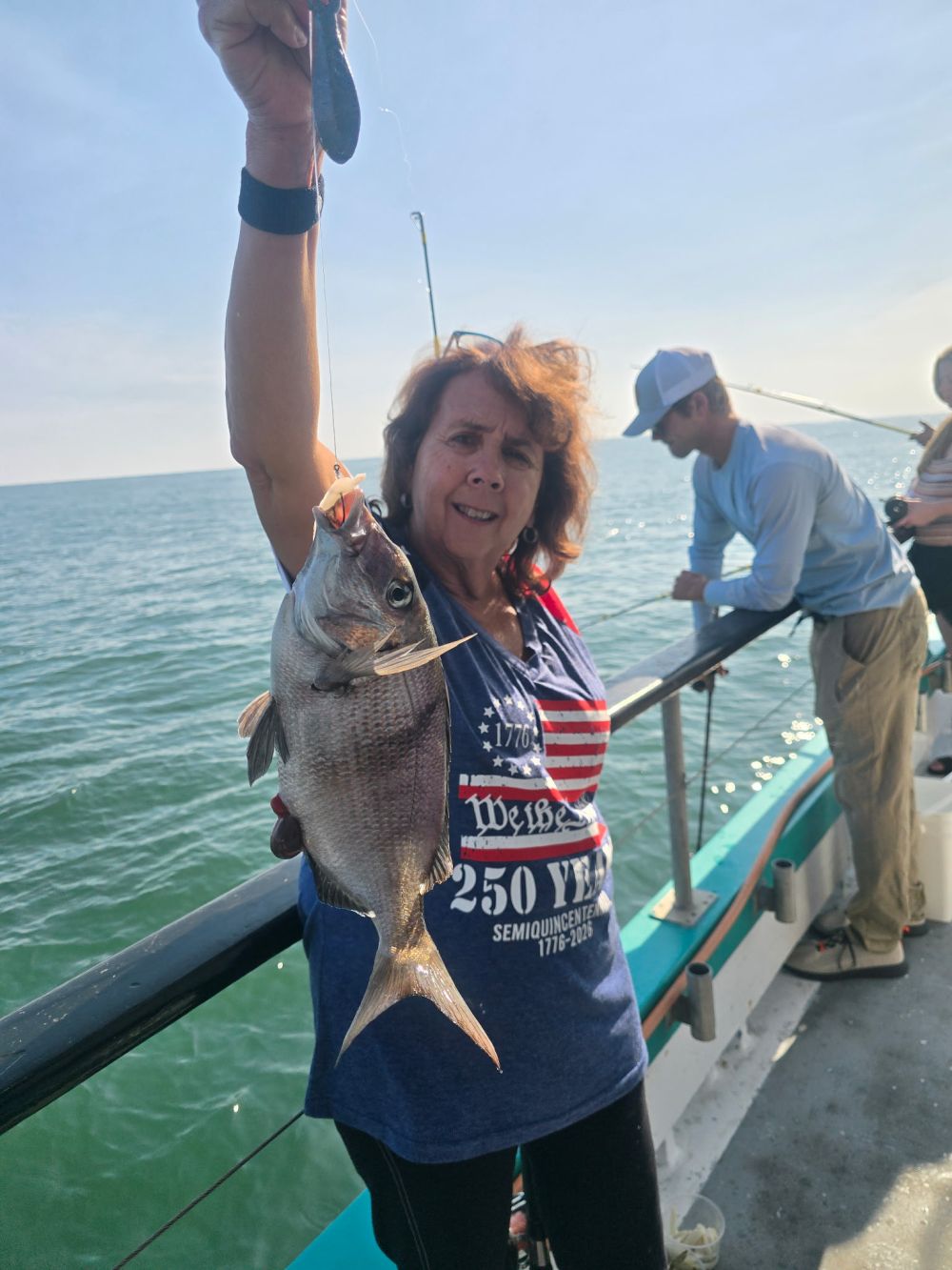 Person holds a fish on a boat with others fishing.