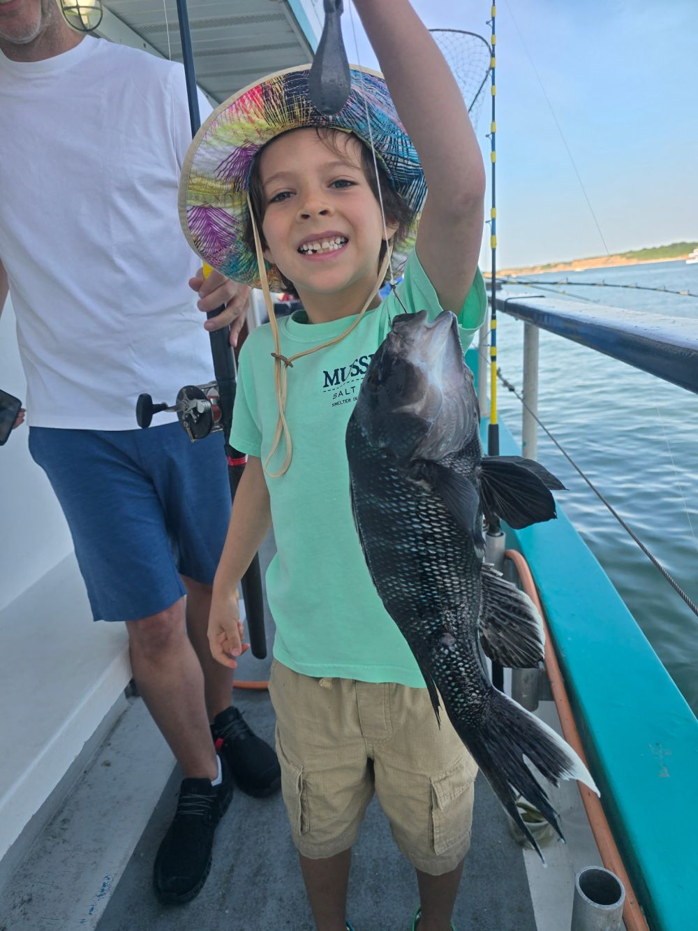 Child smiling, holding a fish on a boat.
