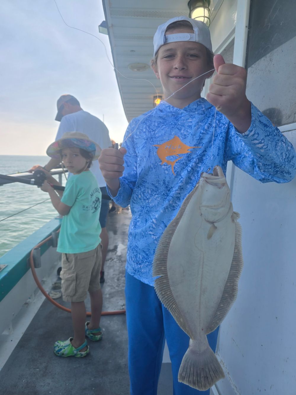 Young boy proudly holding a flounder on a fishing boat.