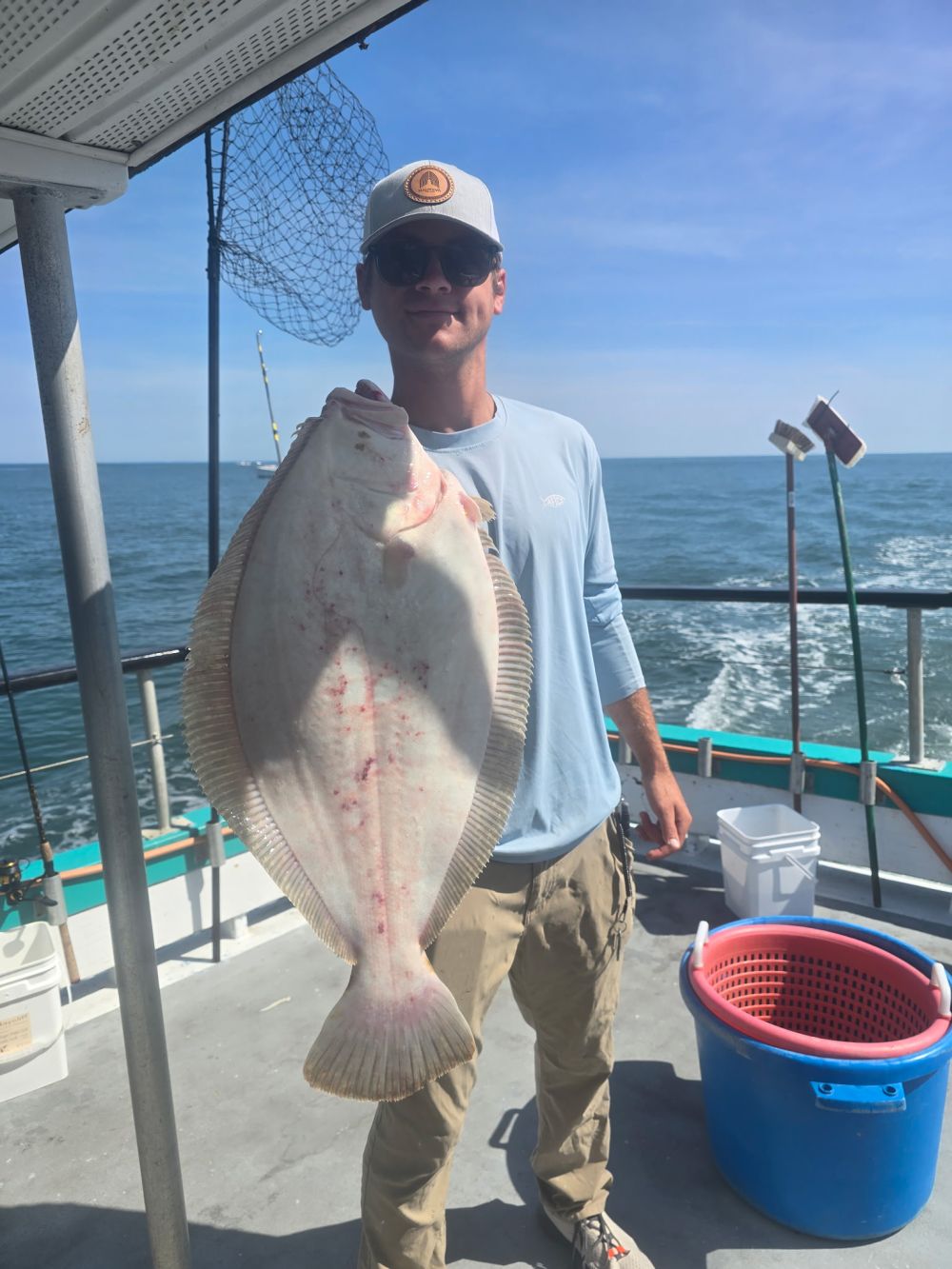 Person holding a large fish on a boat with ocean in the background.