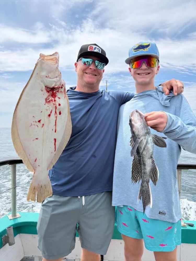 Two people on a boat holding a large fish and a smaller fish, smiling at the camera.