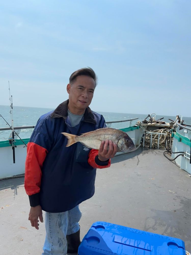Person holding a fish on a boat with ocean in the background.