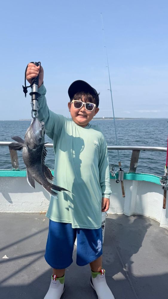 Child holding a fish on a boat, wearing sunglasses and a hat.