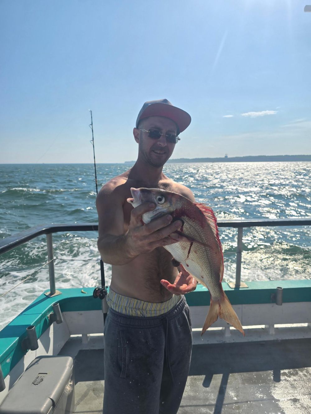 Man on boat holding a large fish with ocean in background.