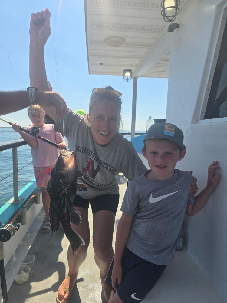 Smiling woman holds fish on boat, with two kids nearby.