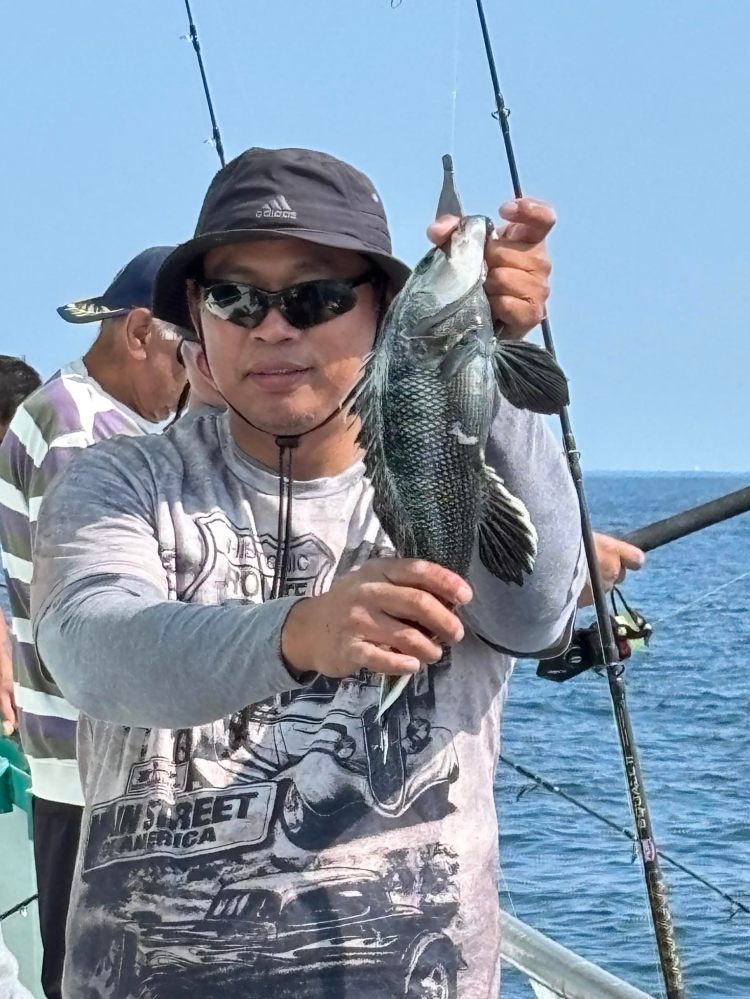 Person holding a fish on a boat, wearing a hat and sunglasses.