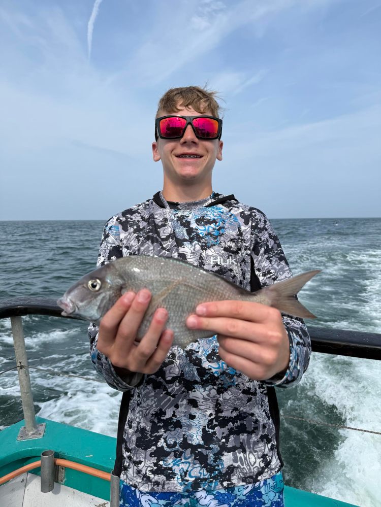 Person holding a fish on a boat with ocean in background.