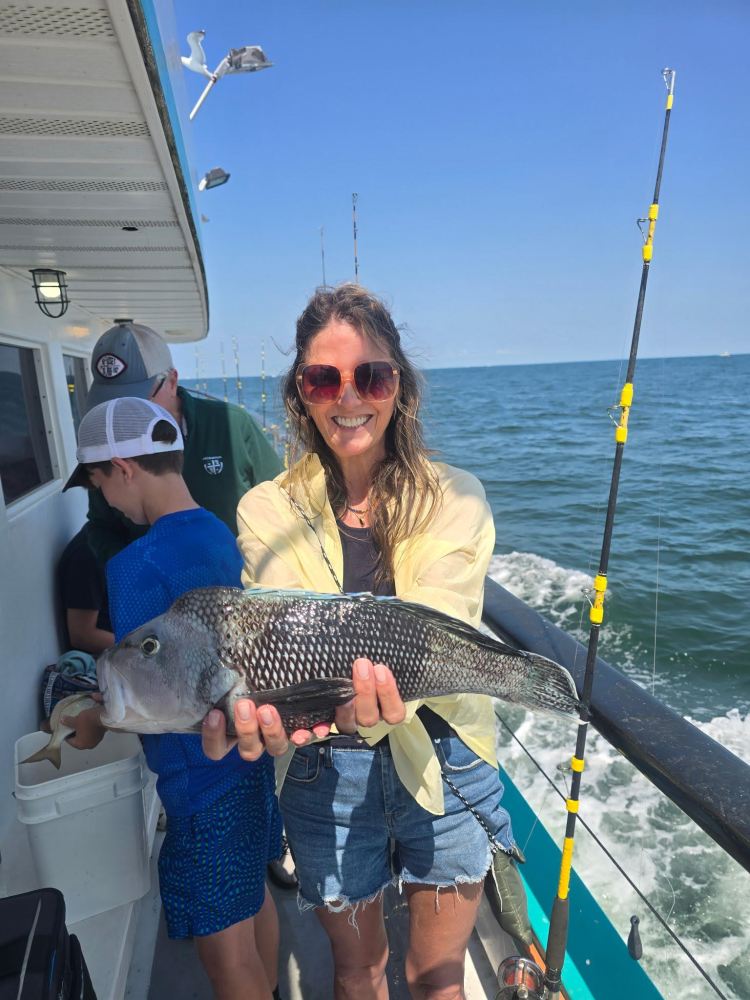 Smiling woman holding a fish on a boat with ocean in the background.