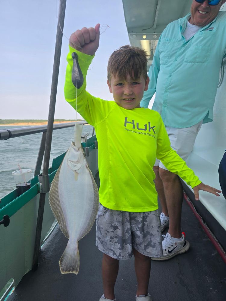 Child in bright shirt holding a fish on a boat with an adult nearby.