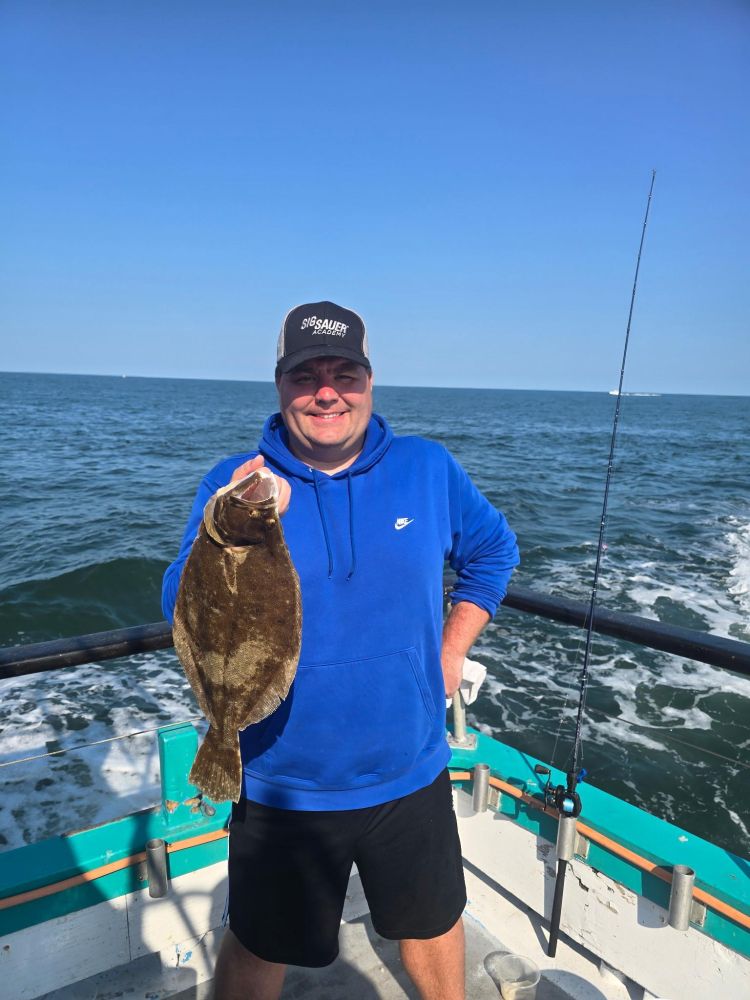 Man smiling, holding a flatfish on a boat with ocean in background.