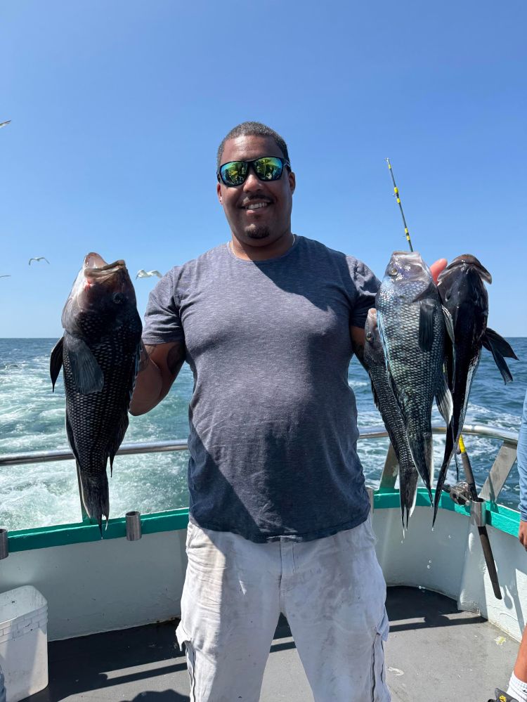 Man on boat holding two large fish with ocean in background.