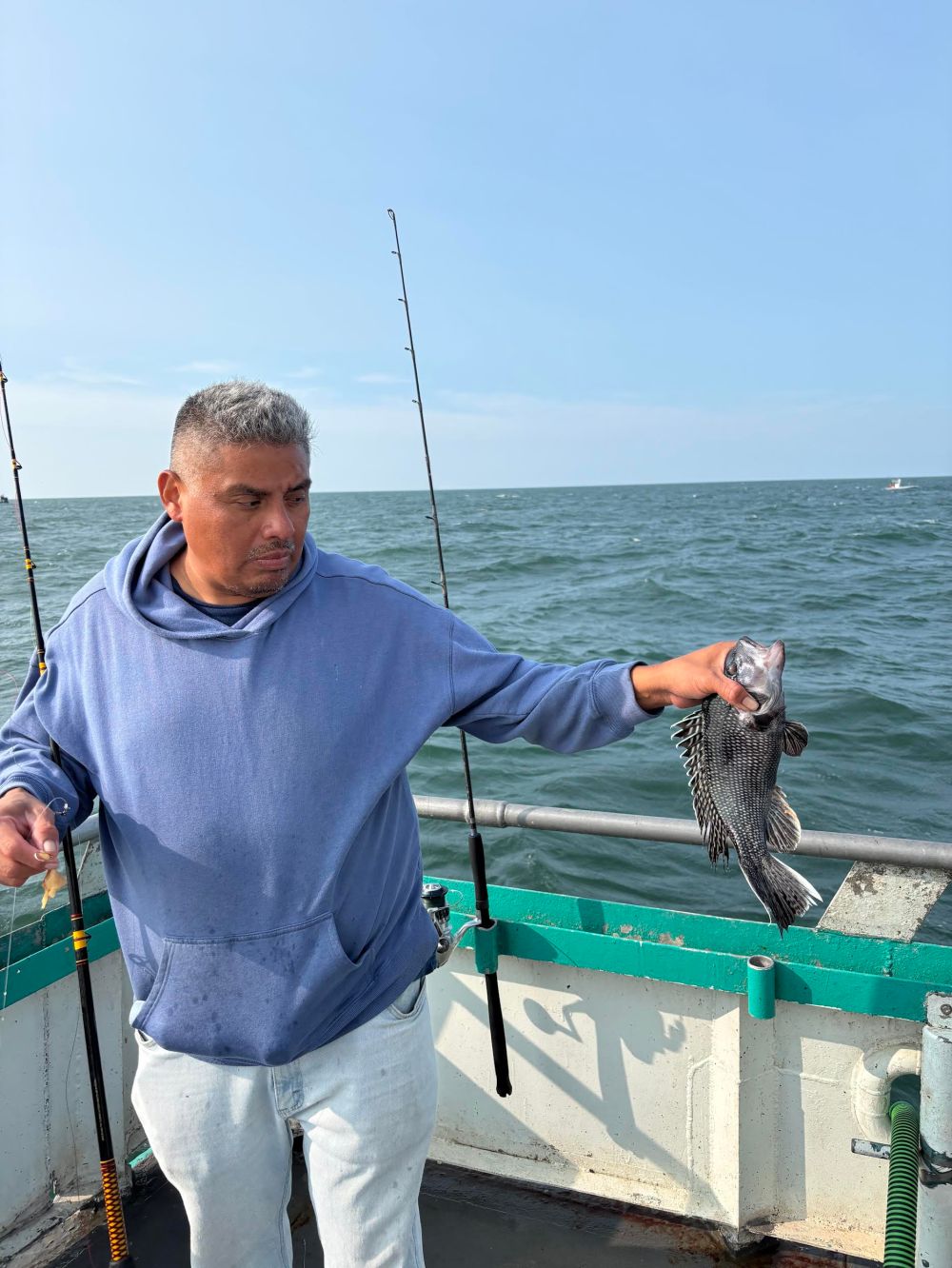Man on boat holding a fish with two fishing rods visible.