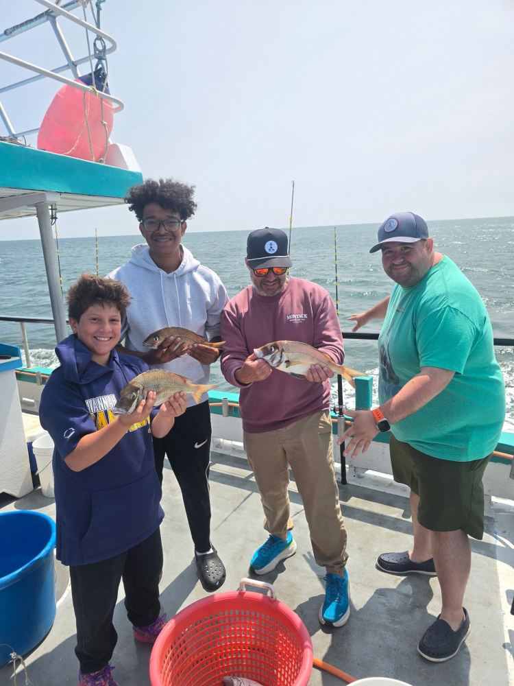 Four people on a boat holding fish they caught, smiling at the camera.