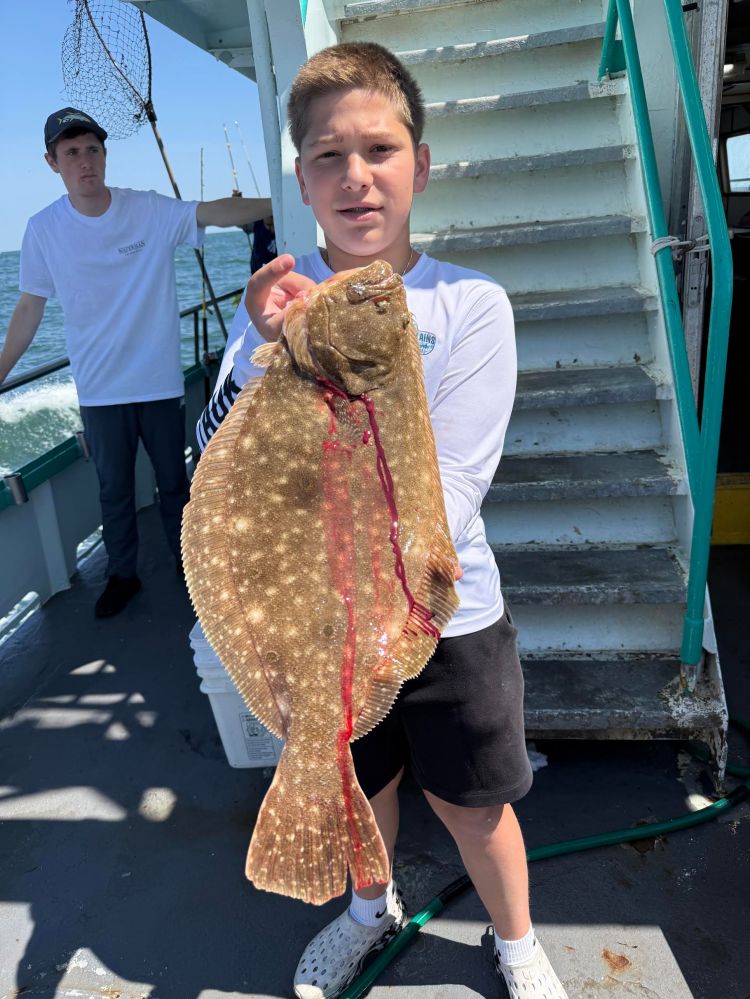Boy holding a large fish on a boat, with another person in the background.