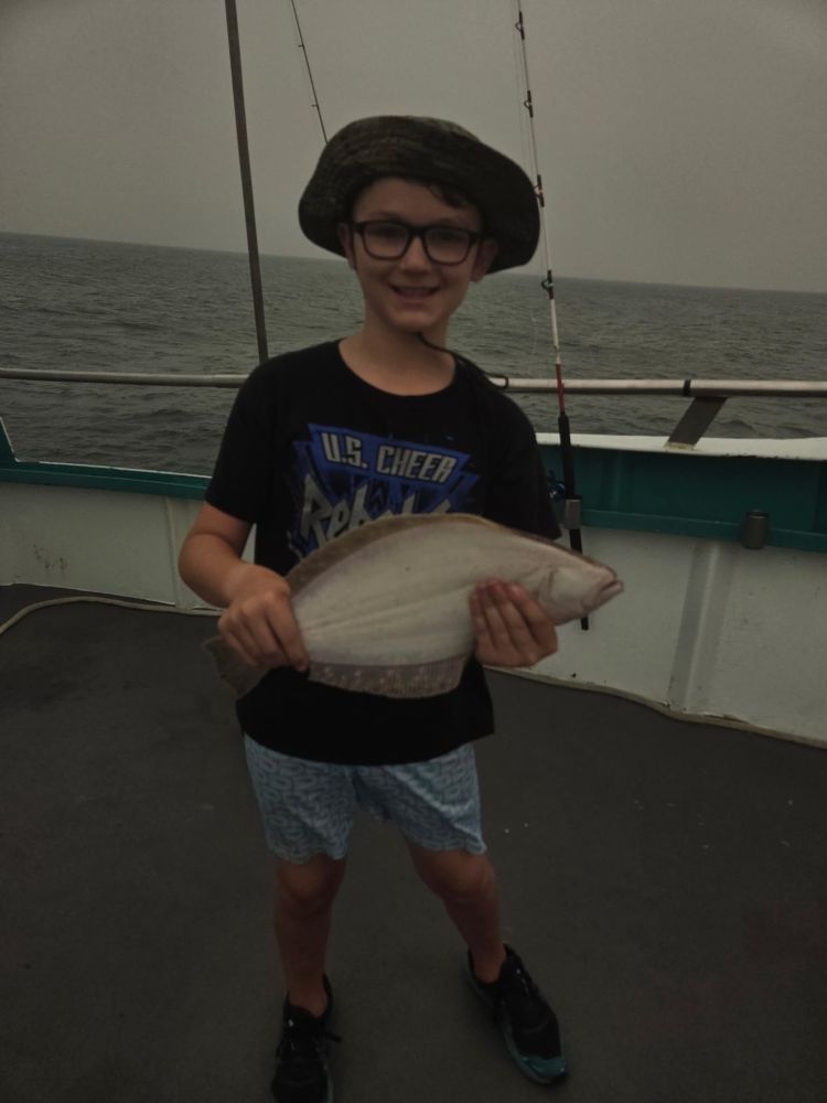 Boy wearing a hat holding a fish on a boat.