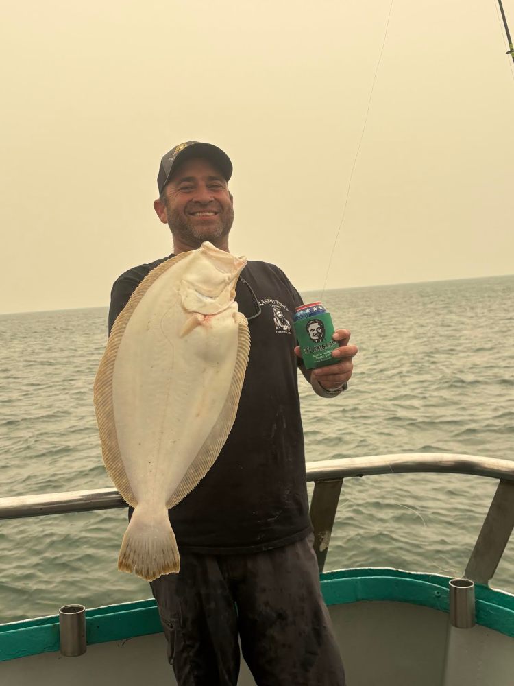 Man holding a large fish and a drink can on a boat.