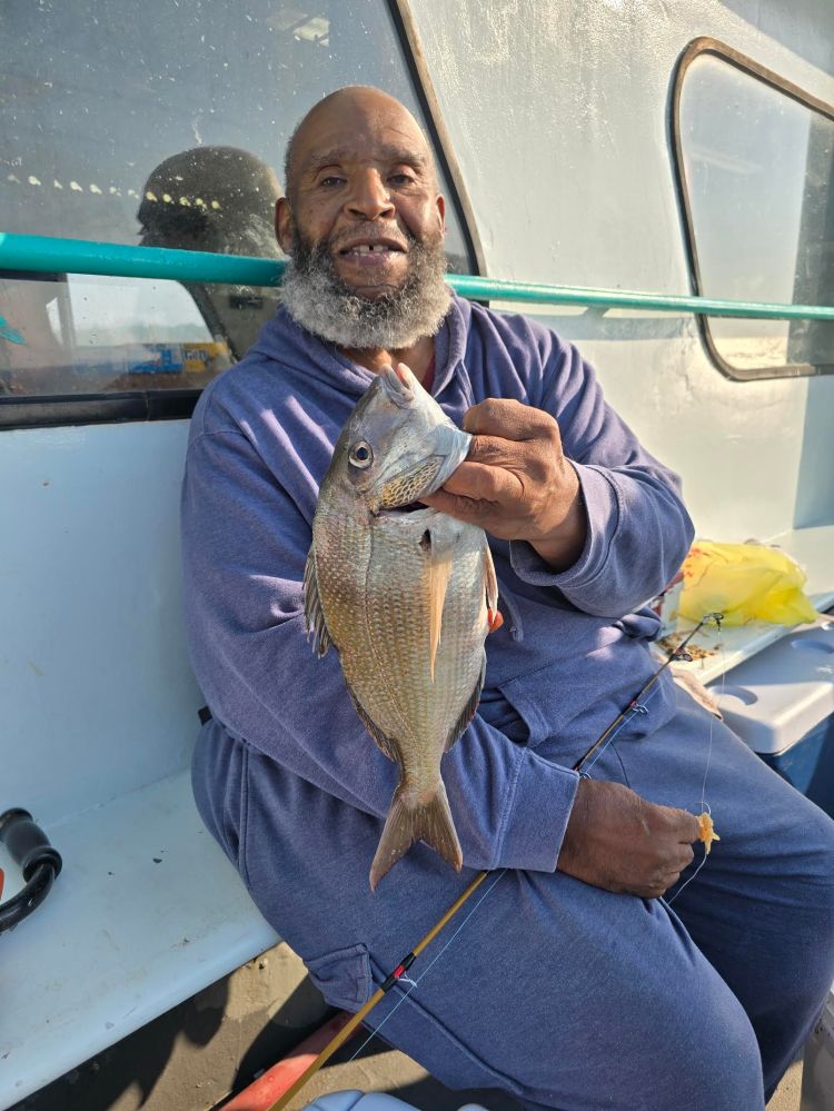 Man in blue outfit holding a fish on a boat seat.